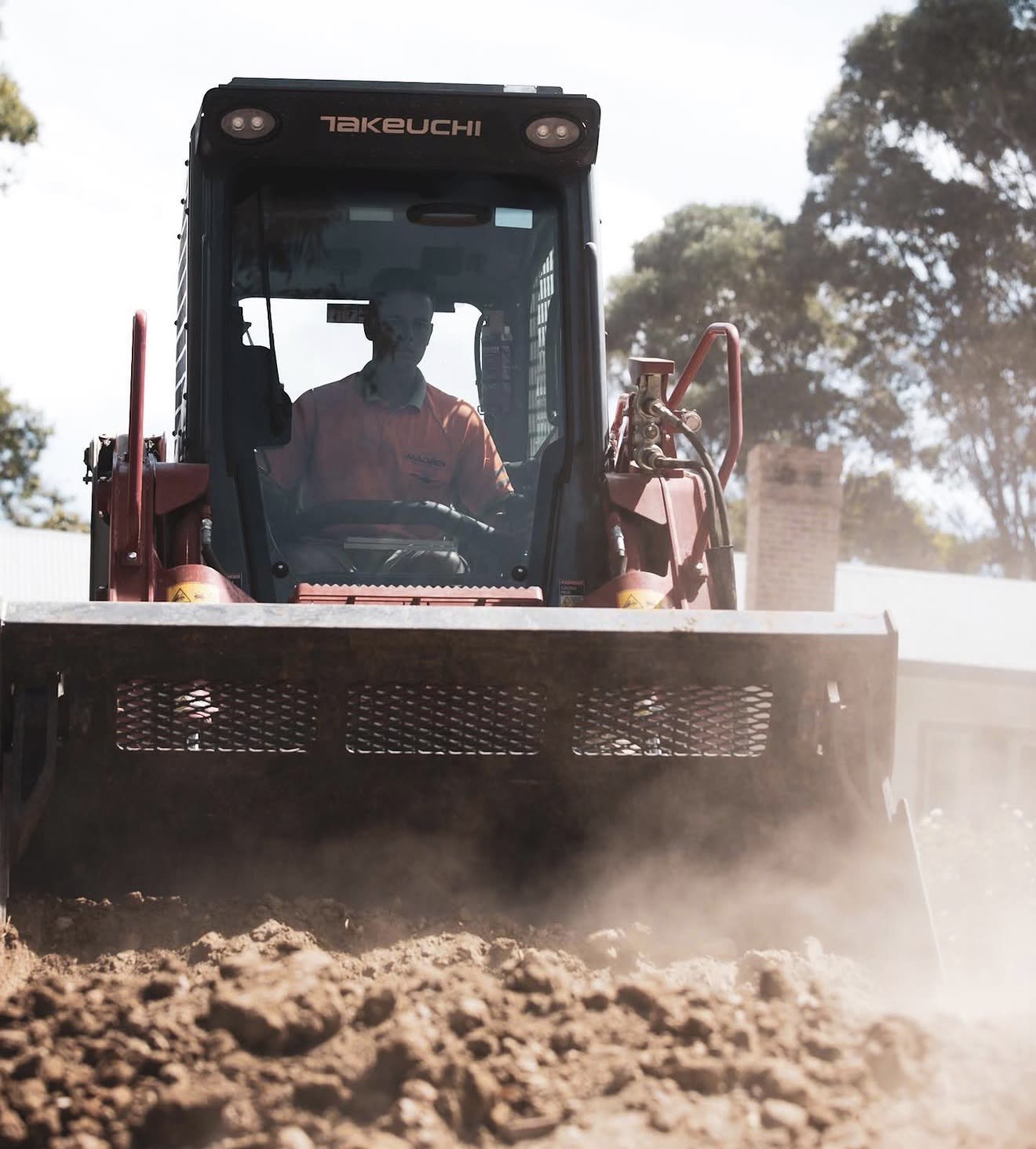 Takeuchi skid-steer POV shot, operator pushing earth with dust kicking up